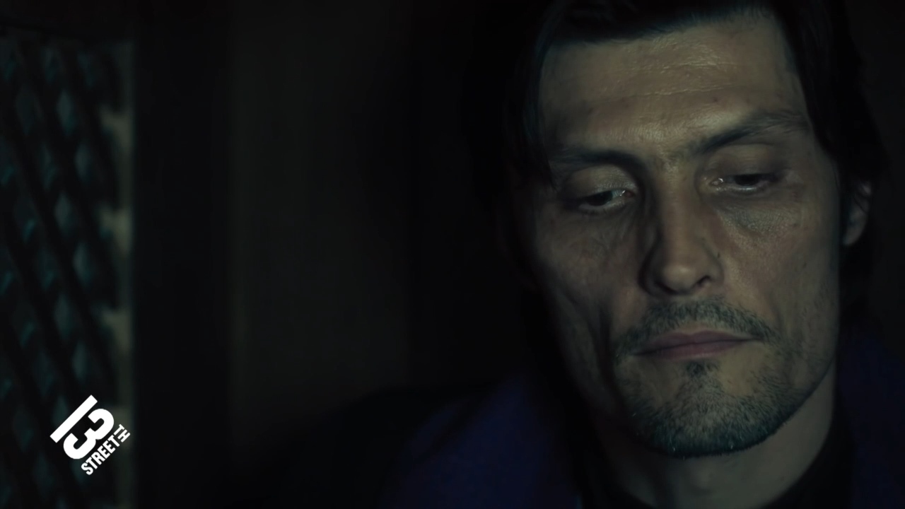 A priest looks down in a dark room.