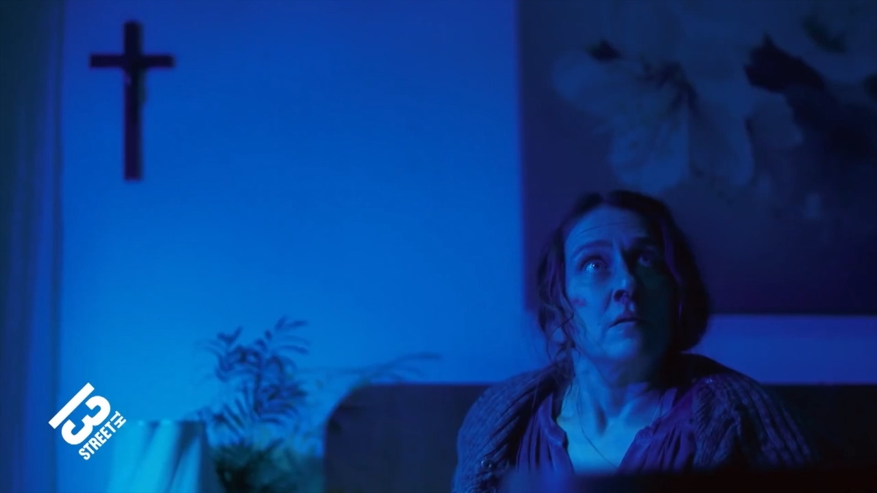 A woman looks up in a blue-lit room.
