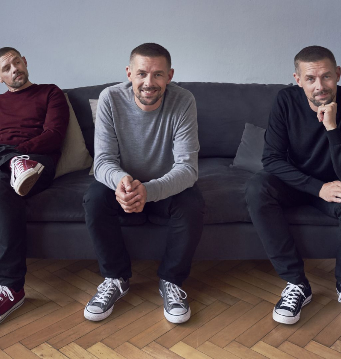 Three men sit together on a sofa.