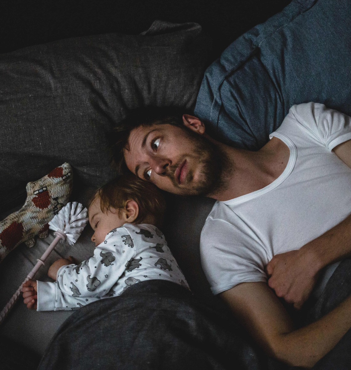 A man lies in bed beside a sleeping baby.