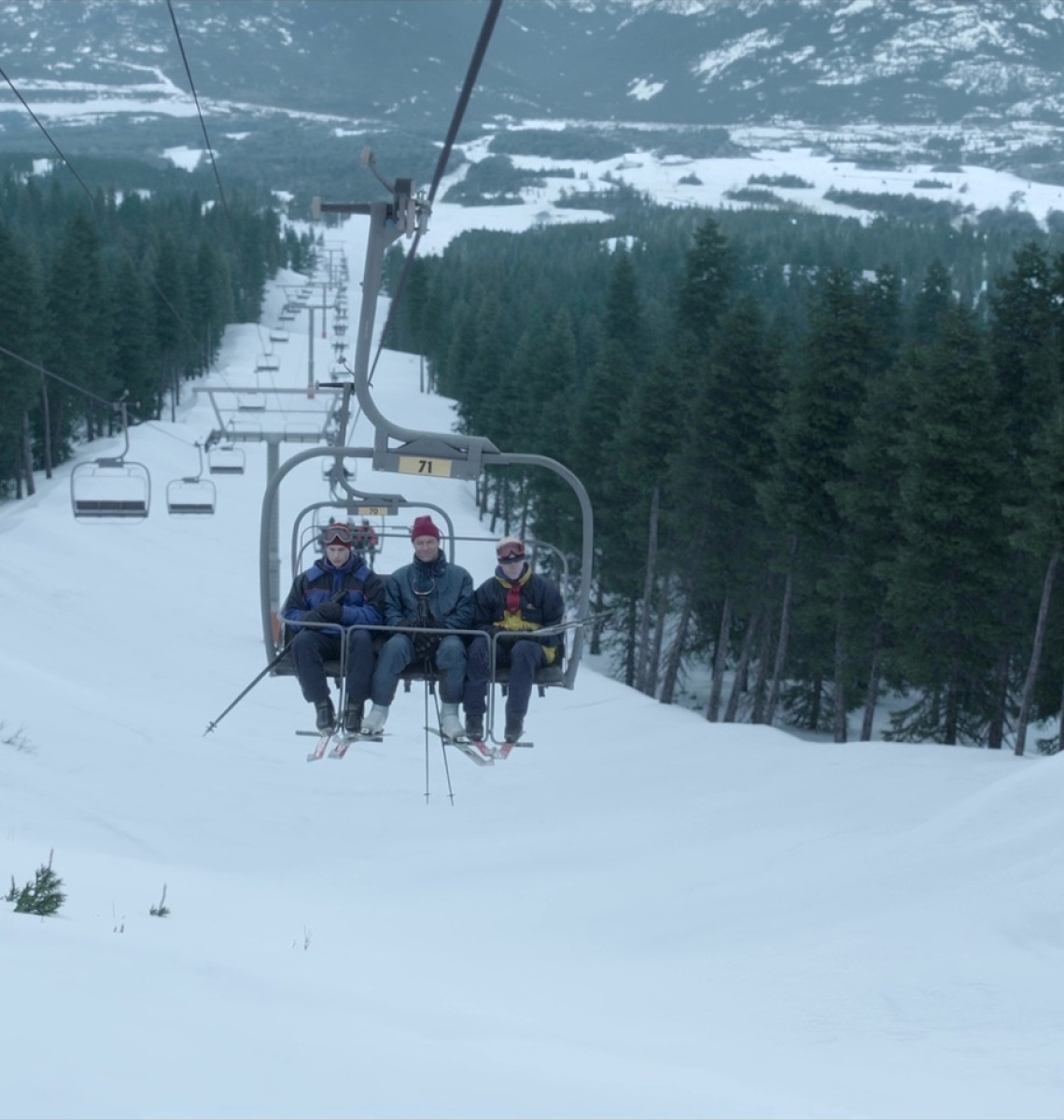Three people ride a chairlift above a snowy forest.