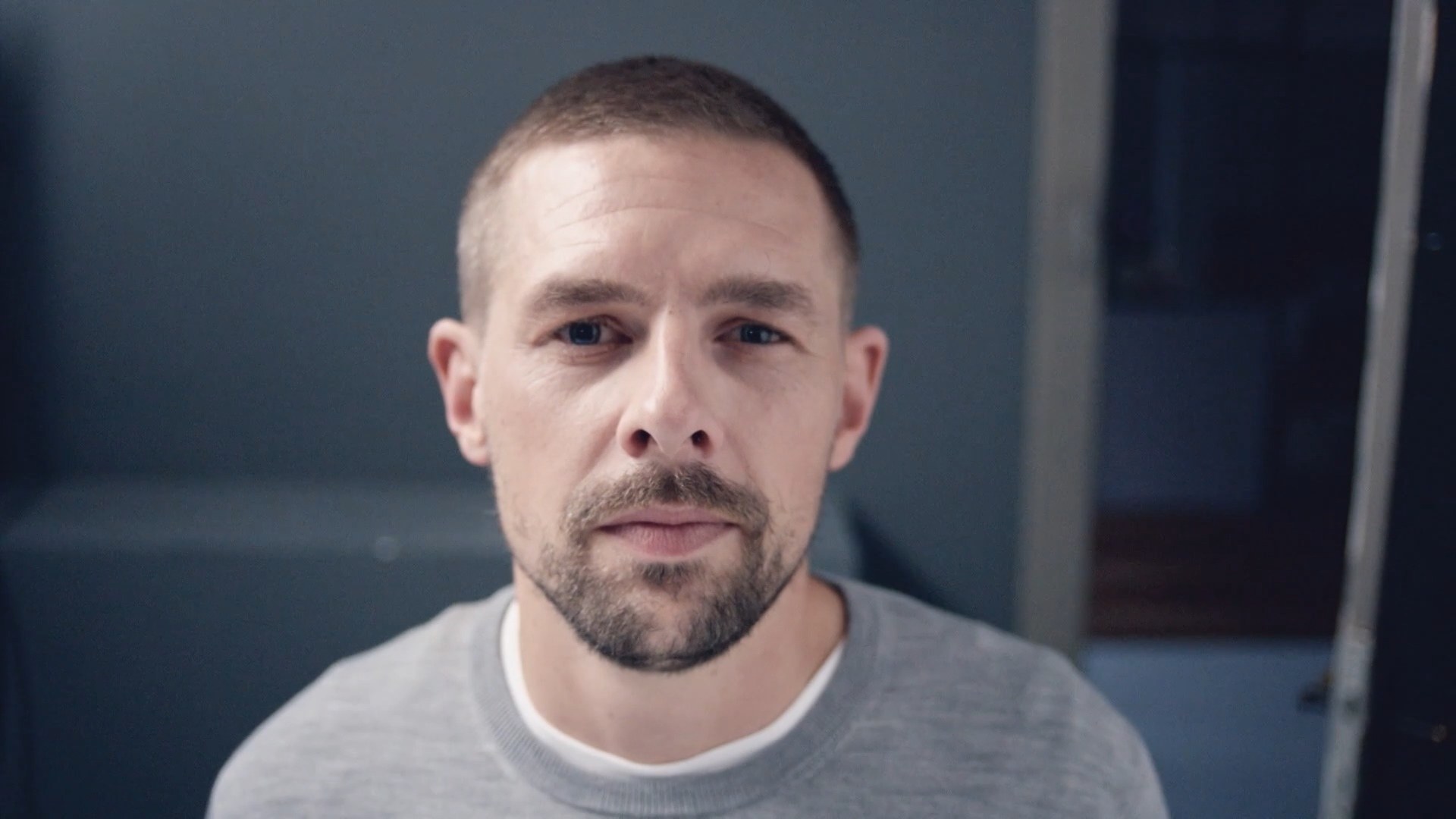 Close-up portrait of a man in front of a blue-grey wall.