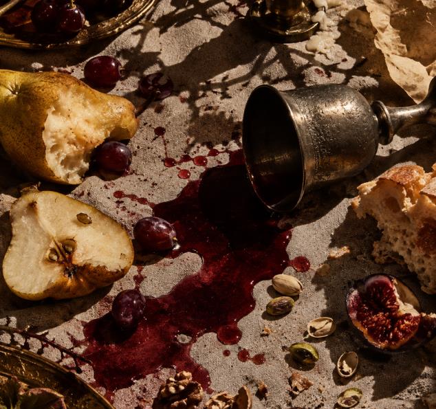 Historical still life with spilled red wine, fruit and a tipped silver goblet.